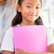 Little asian girl smiling and holding books at home