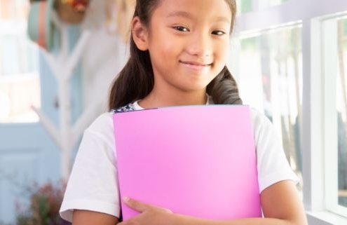 Little asian girl smiling and holding books at home