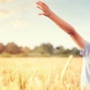 Boy in a wheat field in summer with raised arms watching the sunset