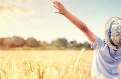 Boy in a wheat field in summer with raised arms watching the sunset