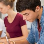 Group of college students studying in classroom writing notes during lesson. Focused guy and girls studying in college library sitting at desk. Group of multiethnic university students doing research sitting in a row.