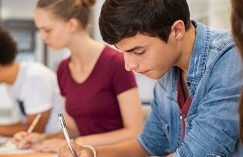 Group of college students studying in classroom writing notes during lesson. Focused guy and girls studying in college library sitting at desk. Group of multiethnic university students doing research sitting in a row.