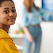 Happy college student sitting in school-desk and looking in camera.