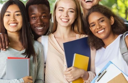 Group of international happy students with books and notebooks having fun in park after studying, smiling at camera