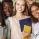 Group of international happy students with books and notebooks having fun in park after studying, smiling at camera