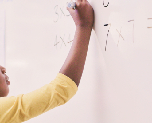 A young black boy enthusiastically writing a math problem on a whiteboard, fully engaged in his learning process.