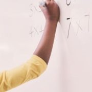 A young black boy enthusiastically writing a math problem on a whiteboard, fully engaged in his learning process.