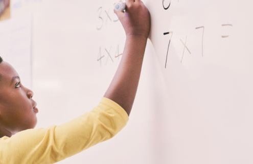 A young black boy enthusiastically writing a math problem on a whiteboard, fully engaged in his learning process.