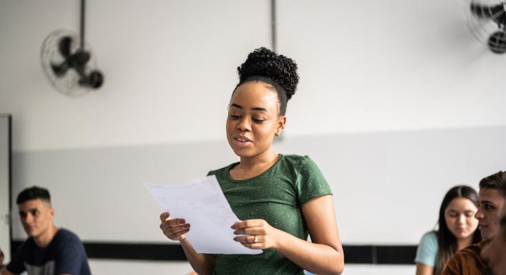 An African American high school student confidently reading her essay aloud to the class, showcasing her communication skills and academic prowess.