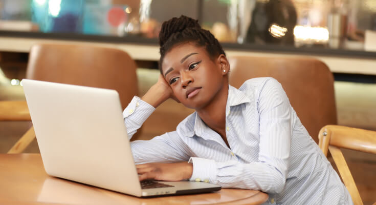 Middle school age female student sits in front of an open laptop, resting her head on her hand, with a bored look on her face.