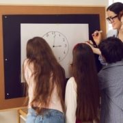 Students working together around a white board featuring a drawing of a clock