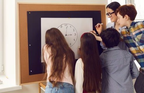 Students working together around a white board featuring a drawing of a clock