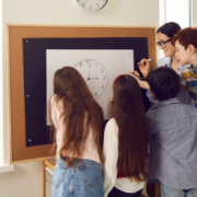 Students working together around a white board featuring a drawing of a clock