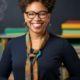 Smiling teacher looking at camera. The teacher is a Black woman wearing glasses and a thin scarf.