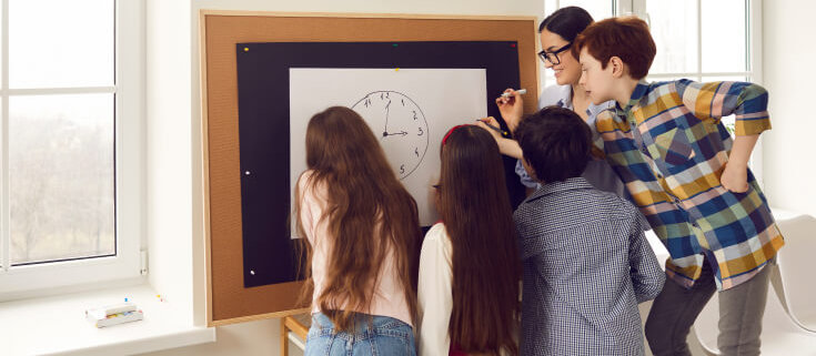 Students working together around a white board featuring a drawing of a clock