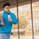 Middle school boy in blue sweatshirt and holding a backpack is running in front of the school as if he's late