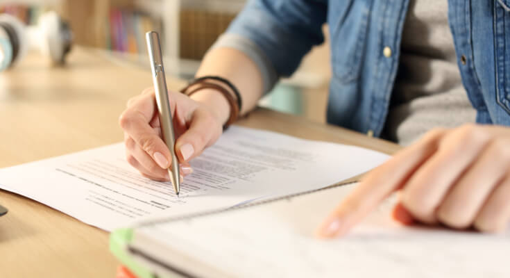 Close up of a student's hands as they follow one line of handwritten notes with one hand and write notes with the other hand.