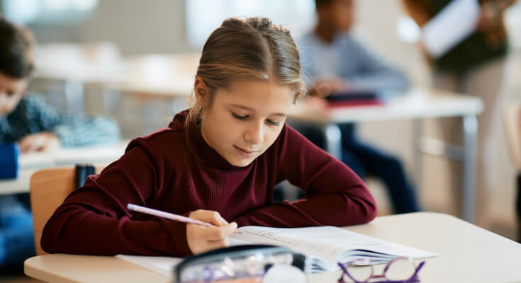 Young, female middle school student sits at her desk holding a pencil over a textbook. She is practicing active reading.