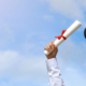 Man's arms raised against a blue sky holding a graduation cap and rolled diploma