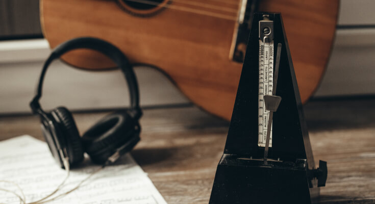 A metronome sits on a table with headphones and a piece of paper behind it.