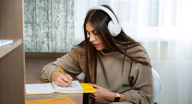 Teen girl student focuses on her homework by having big white headphones on to eliminate distractions. 