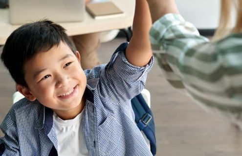 Young male student of Asian heritage smiles as he high-fives his academic coach standing in front of him.