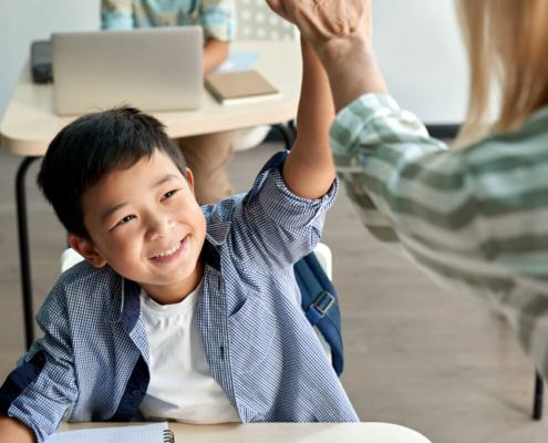 Young male student of Asian heritage smiles as he high-fives his academic coach standing in front of him.