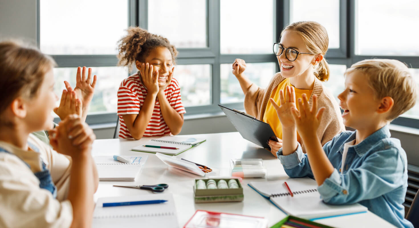 A group of elementary school students sit around a table with an educator and engage in positive, team-based learning.