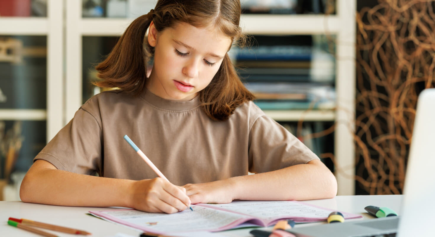 Middle school female student sits at a table and fills out a test, which she can do confidently thanks to working with an academic coach.