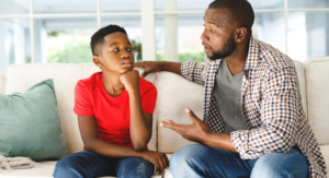 An adult speaks to a young child on the couch while he listens intently.