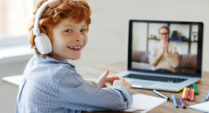 A student wearing headphones looks over his shoulder while in a virtual coaching session on his laptop