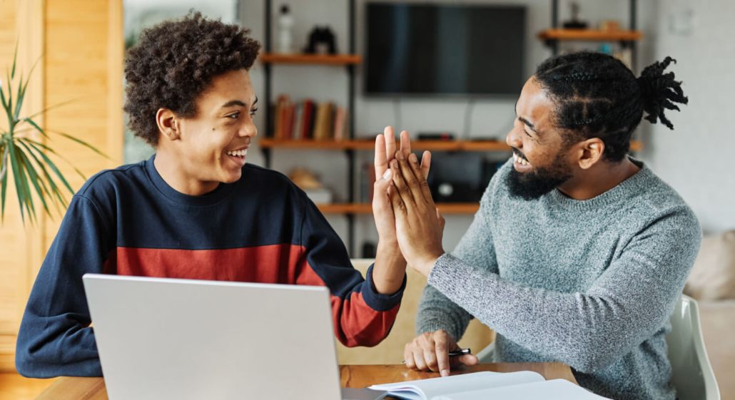 Two young men give each other a high five while working on school work.