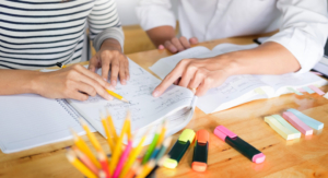 two people point to content on a written page while surrounded by markers