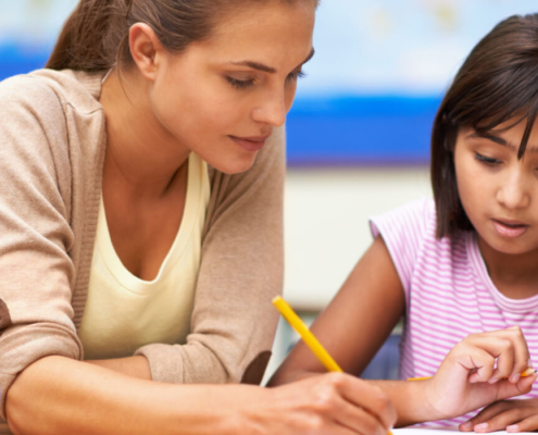 An adult helps a young child in a pink shirt with a written assignment