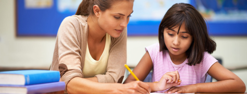 An adult helps a young child in a pink shirt with a written assignment