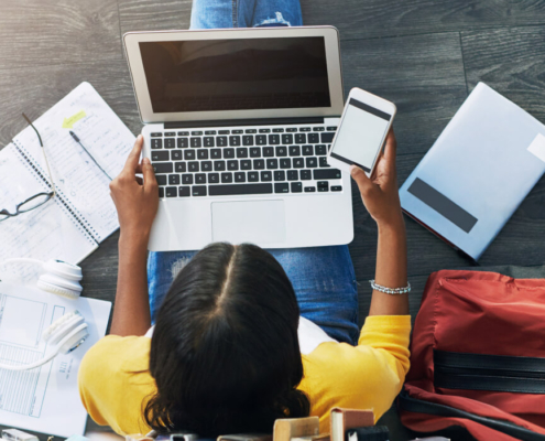 A student sits on the floor among a laptop and paperwork.