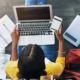 A student sits on the floor among a laptop and paperwork.