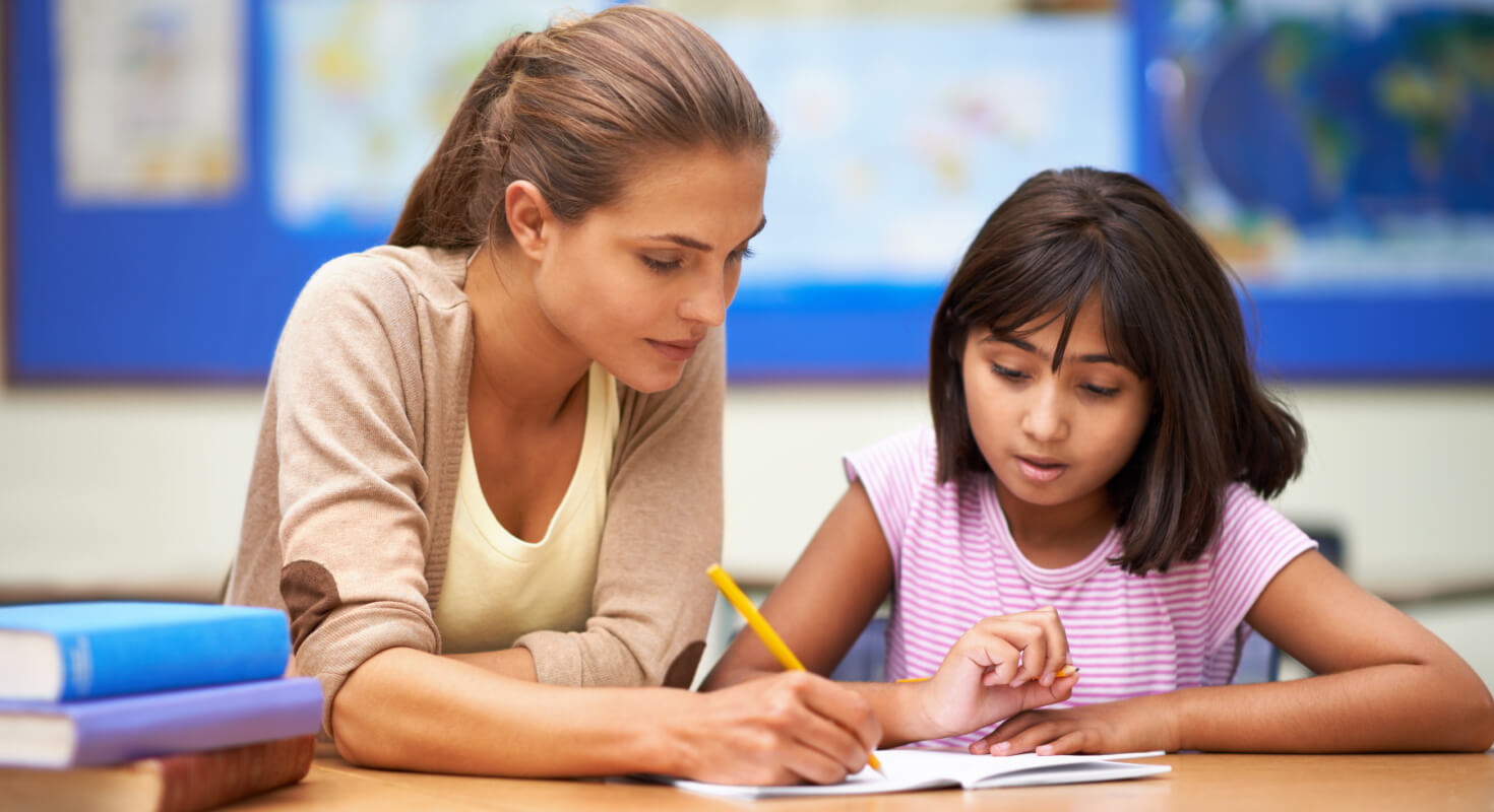 An adult helps a young child in a pink shirt with a written assignment